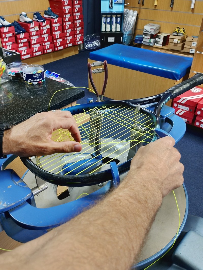 Hands weaving string through a racket held on the stringing machine